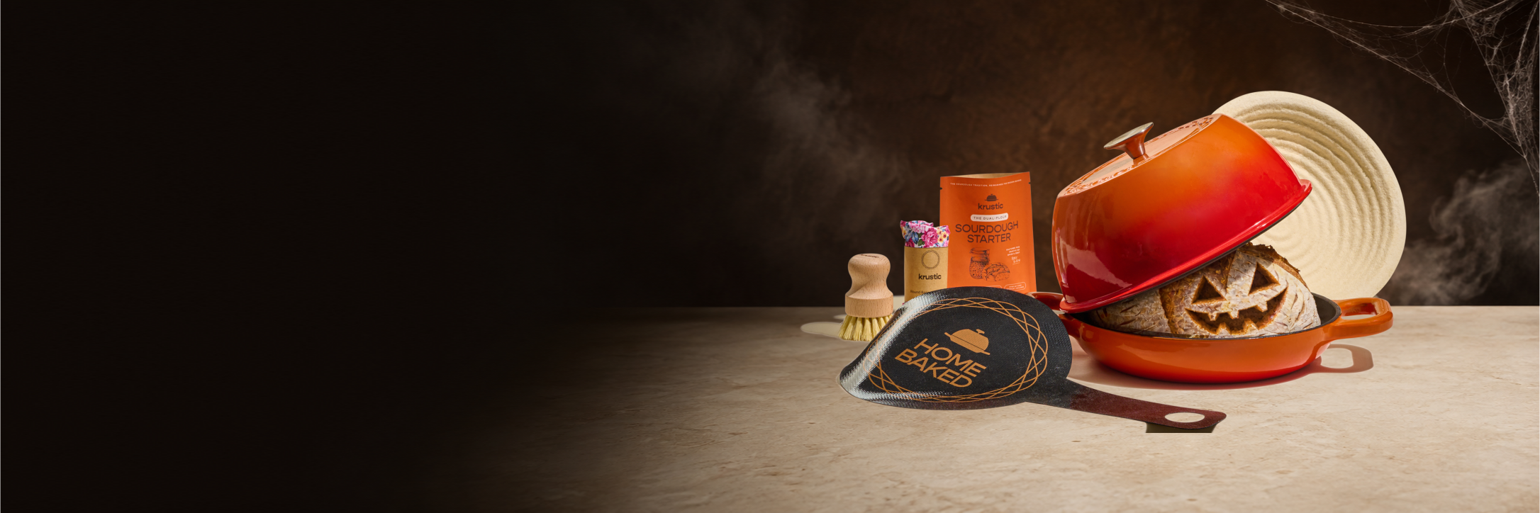Original orange Krustic Boule ensemble with a Halloween sourdough loaf and smoky seasonal backdrop.